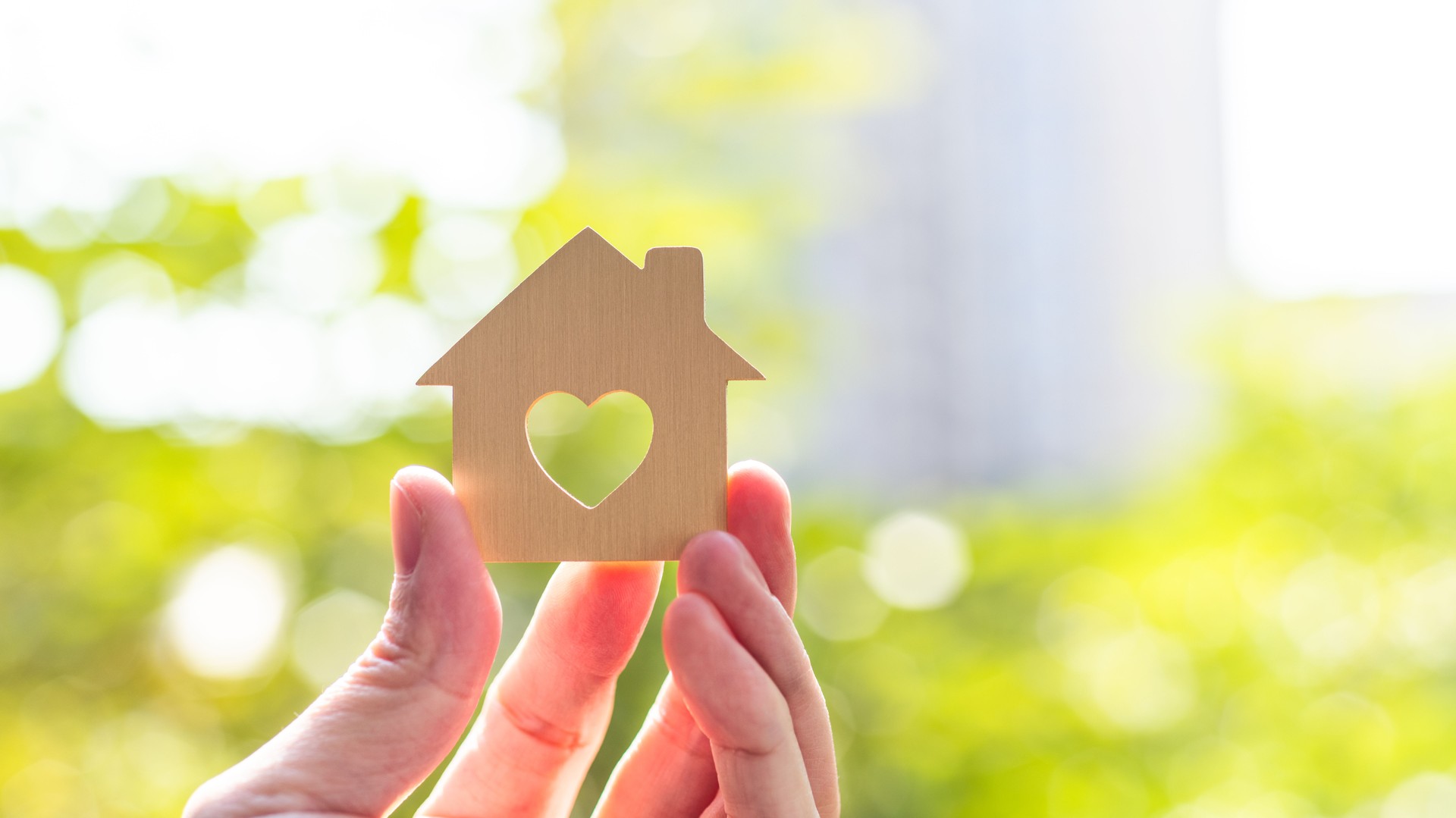 Human hand holding model house with a heart shape